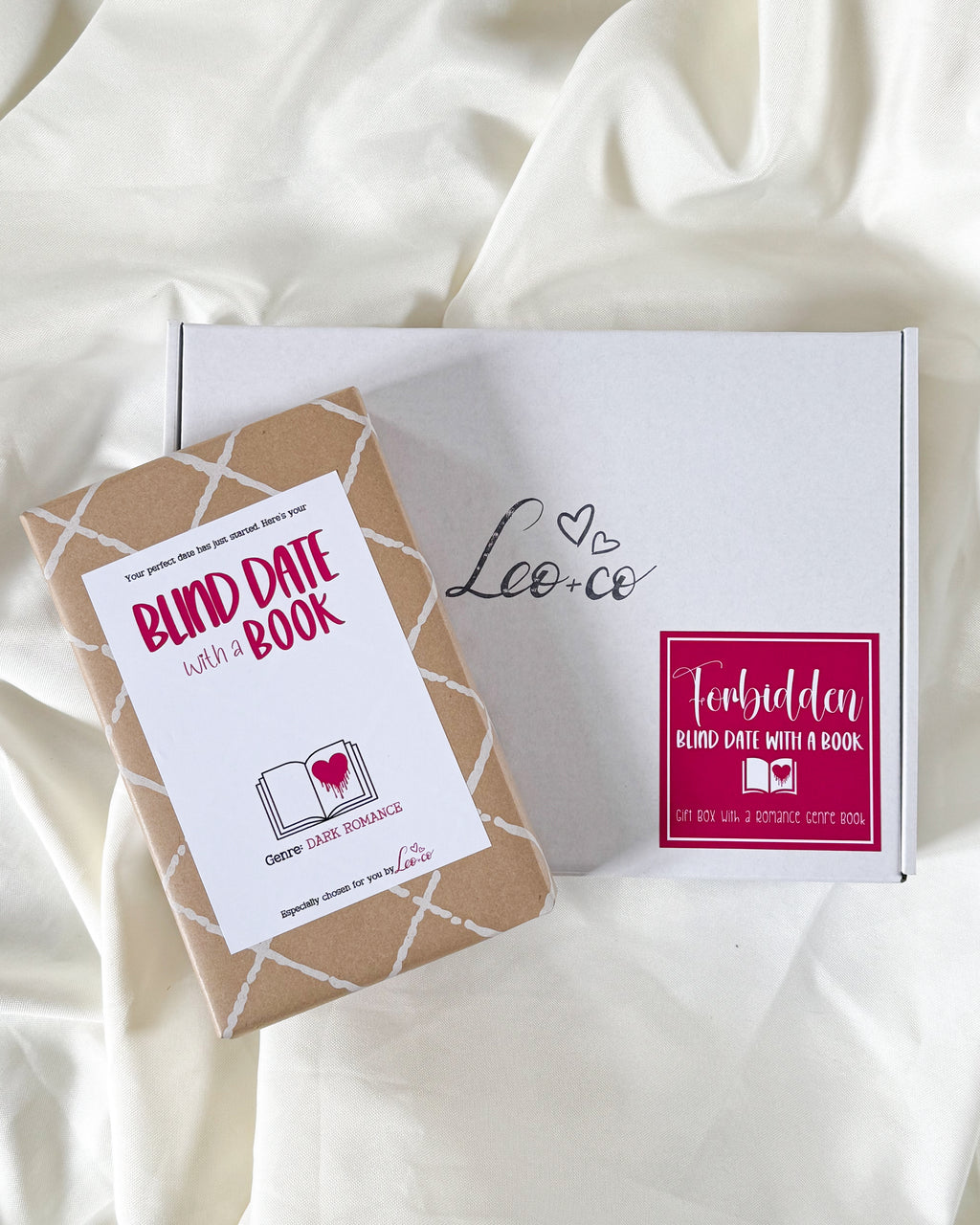 A boxed dark romance blind date with a book product displayed on draped white fabric. The set includes a white box with the brand name 'Leo.