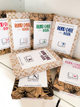 Load image into Gallery viewer, A collection of “Blind Date with a Book” wrapped books displayed on a white shelf, featuring different genres including romance, thriller, fantasy, cosy crime, and historical fiction, wrapped in patterned paper with minimalist genre labels and surprise book packaging.
