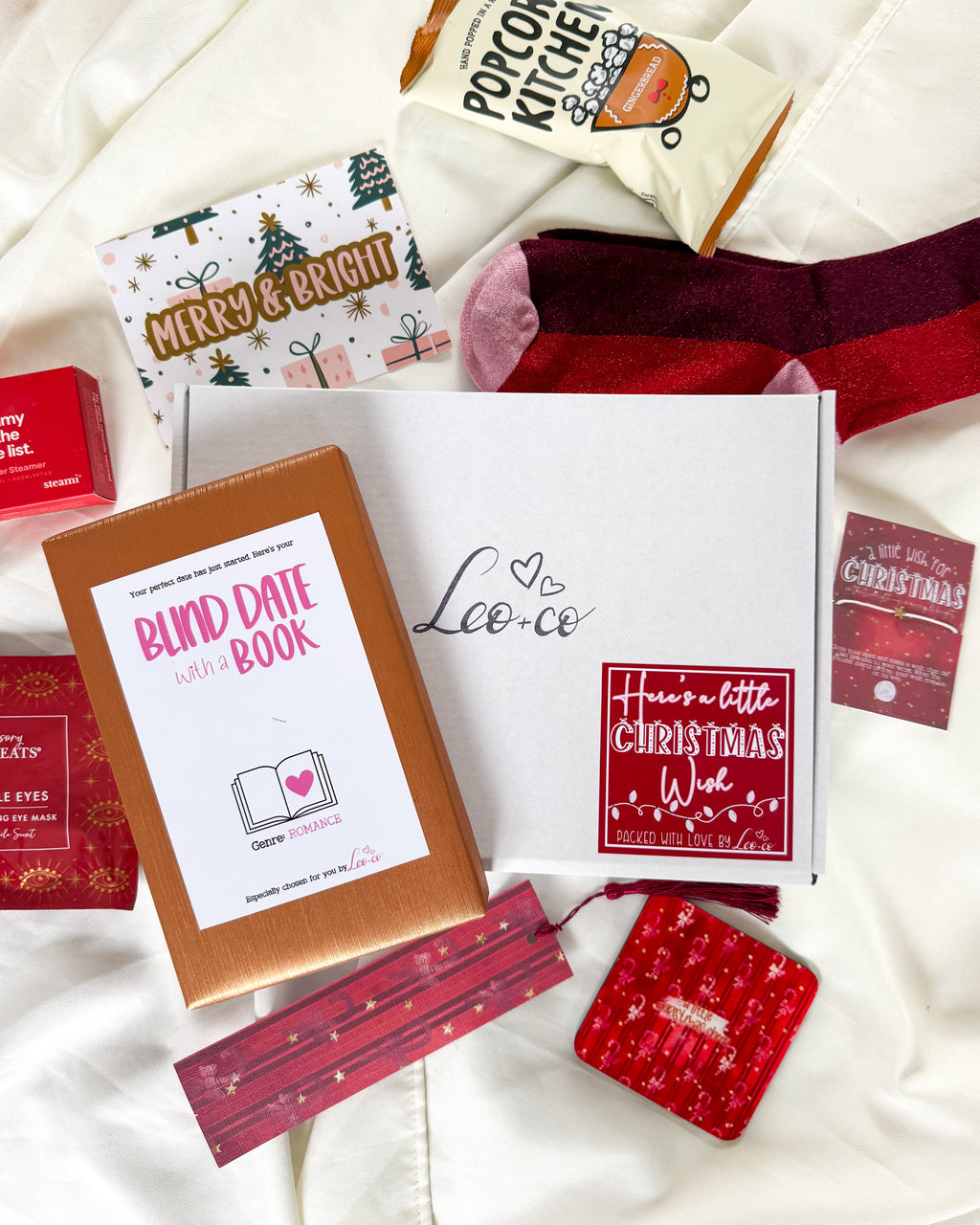 Christmas Blind Date With a Book gift box by Leo + Co, featuring a mystery book, cosy socks, shower steamer, Christmas wish bracelet, festive coaster, bookmark, self-heating eye mask and vegan gingerbread popcorn.