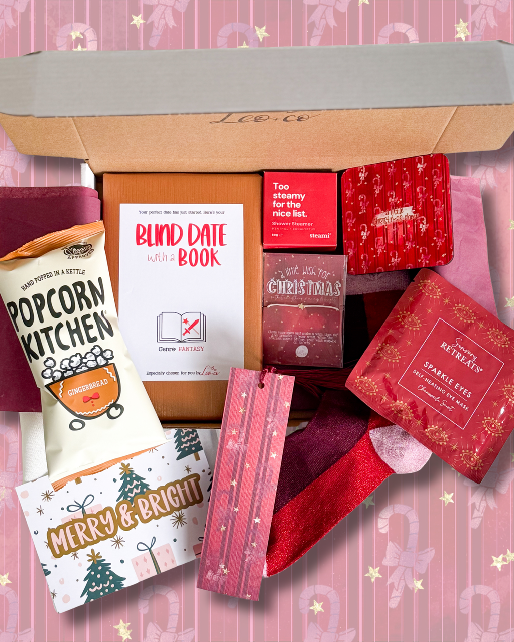 Christmas Blind Date With a Book gift box by Leo + Co, featuring a mystery book, cosy socks, shower steamer, Christmas wish bracelet, festive coaster, bookmark, self-heating eye mask and vegan gingerbread popcorn.